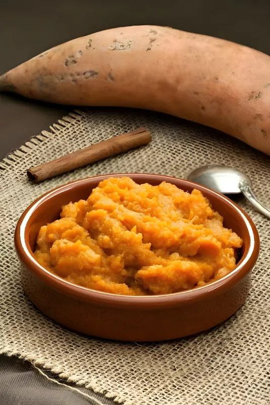 Bowl of mashed sweet potatoes served warm with a cinnamon stick and spoon.