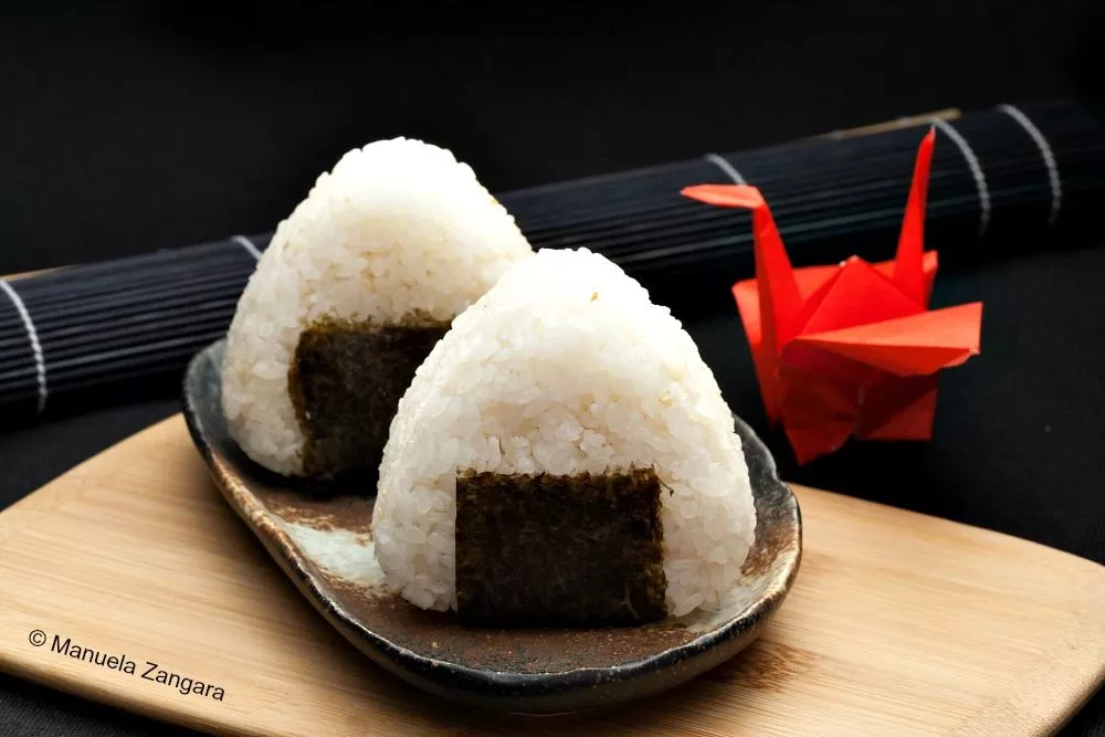 Japanese rice balls shaped into triangles and wrapped with seaweed on a wooden board.