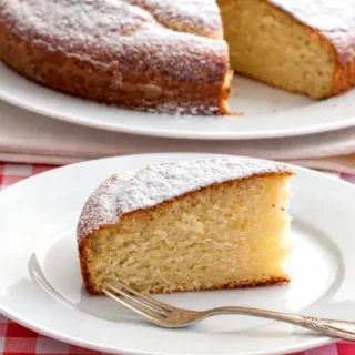 Slice of moist cake dusted with icing sugar served on a white plate with a fork.