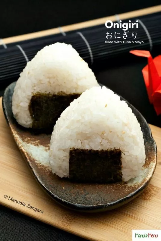 Two triangle rice balls wrapped with nori, served on a plate.