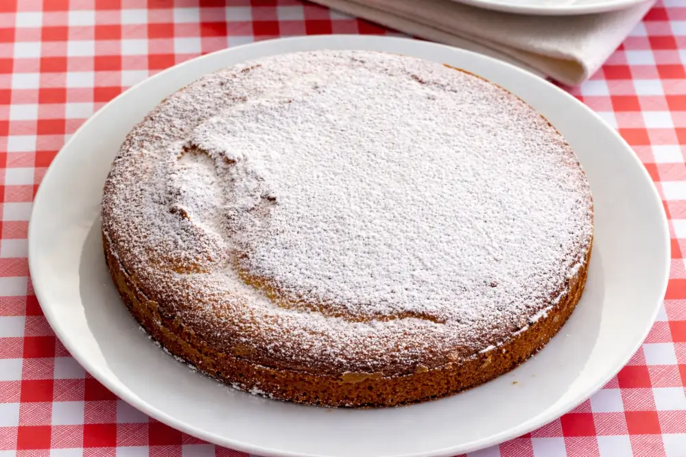 Whole vanilla cake topped with icing sugar placed on a serving plate.