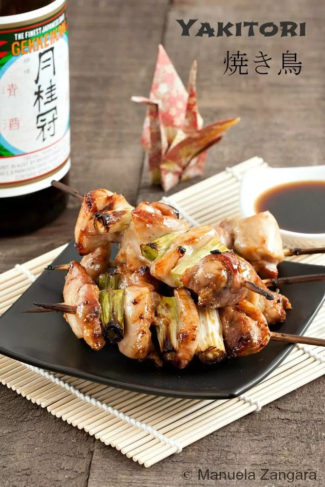 Japanese grilled chicken skewers with sauce, served on a black plate.