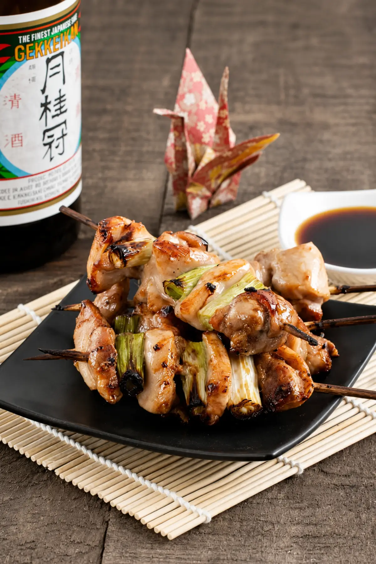 Yakitori chicken skewers with grilled spring onions served on a black plate.