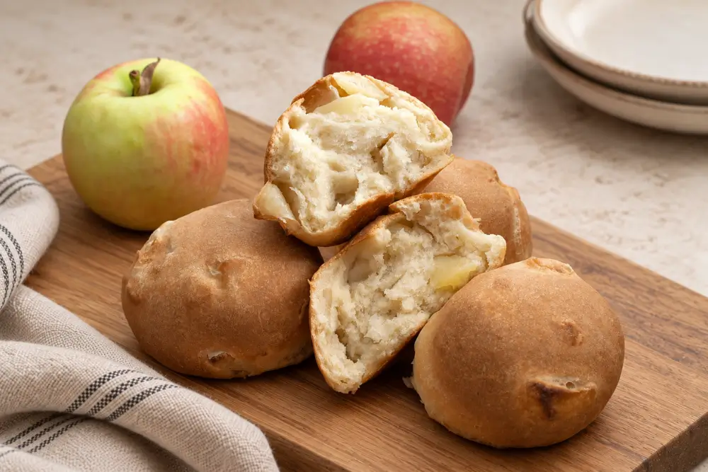 Homemade apple rolls served on a wooden board with two fresh apples.