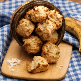 Banana Coconut Cookies with golden brown edges served in a coconut shell beside a ripe banana.