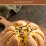 Homemade pumpkin shaped bread topped with pumpkin seeds on a wooden serving board.