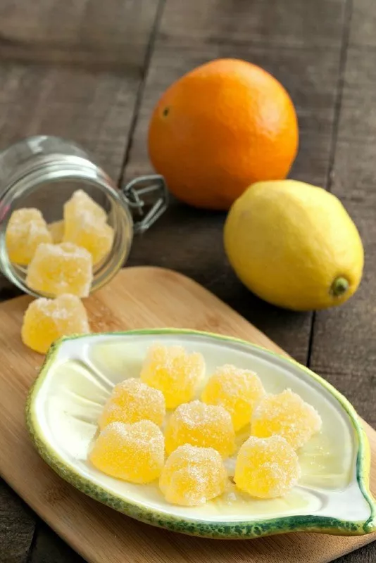 Homemade orange and lemon jelly candies coated in sugar on a plate with fresh citrus in the background.