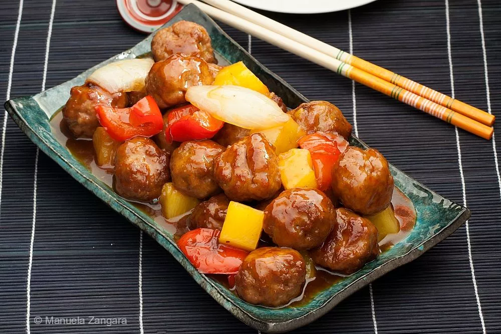 A serving of Chinese sweet and sour pork meatballs with colorful vegetables like red bell peppers and pineapple, arranged on a platter.