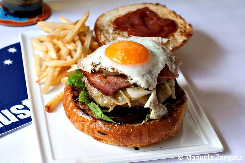 Classic Australian burger topped with fried egg, bacon, and onion, served with fries.
