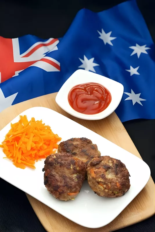 Cooked Australian rissoles on a white plate with grated carrot and tomato sauce, placed over an Australian flag.