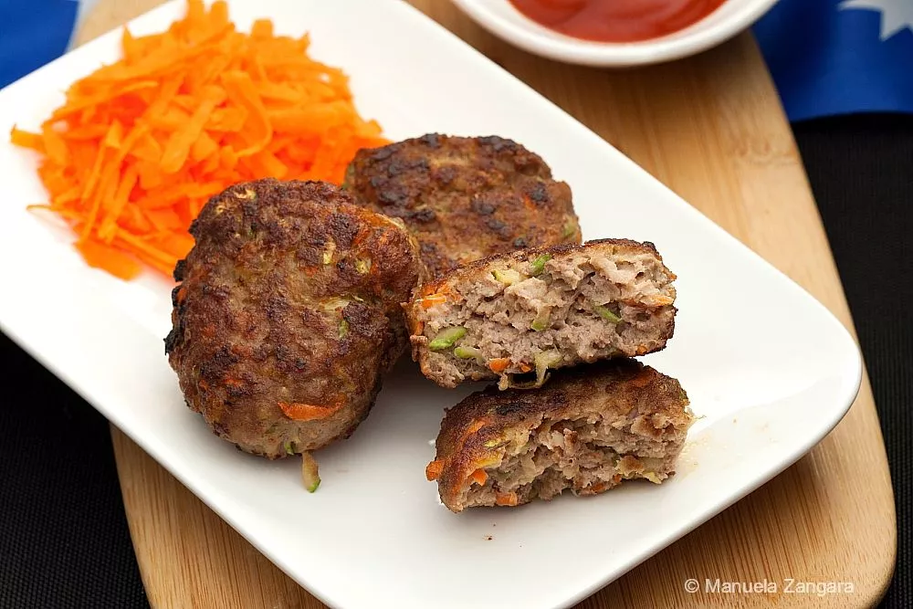 Cooked Australian rissoles with grated vegetables inside, served with carrot and tomato sauce.