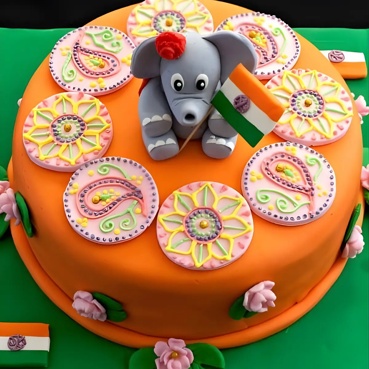 Finished Indian Cake covered in orange fondant, decorated with pink mehndi fondant rounds, lotus flowers, and a fondant elephant holding the Indian flag.