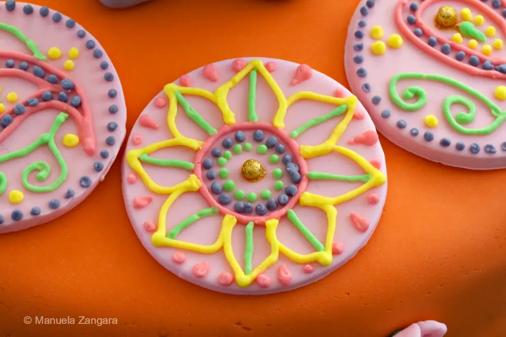Detailed view of a fondant round with a flower-shaped mehndi design in bright icing colours on the orange Indian Cake.