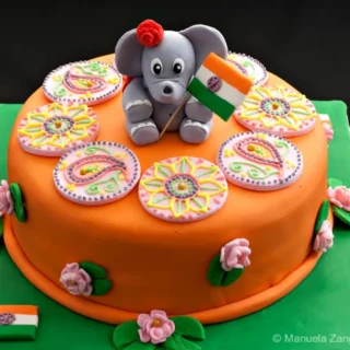 Full view of the Indian Cake covered in orange fondant, topped with a fondant elephant holding the Indian flag and colourful mehndi rounds.