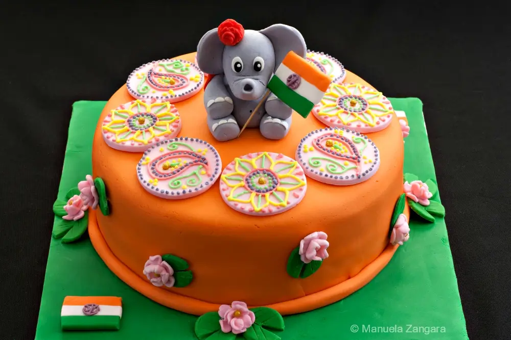 Full view of the Indian Cake covered in orange fondant, topped with a fondant elephant holding the Indian flag and colourful mehndi rounds.