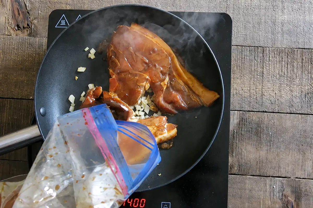 Marinated pork chops and chopped onion cooking together in a frying pan.