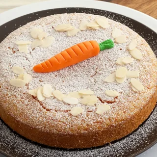 Almond carrot cake on a serving plate with powdered sugar and almond slices.