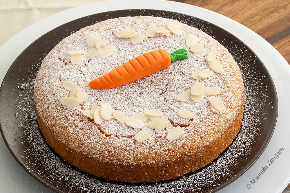 Almond carrot cake on a serving plate with powdered sugar and almond slices.