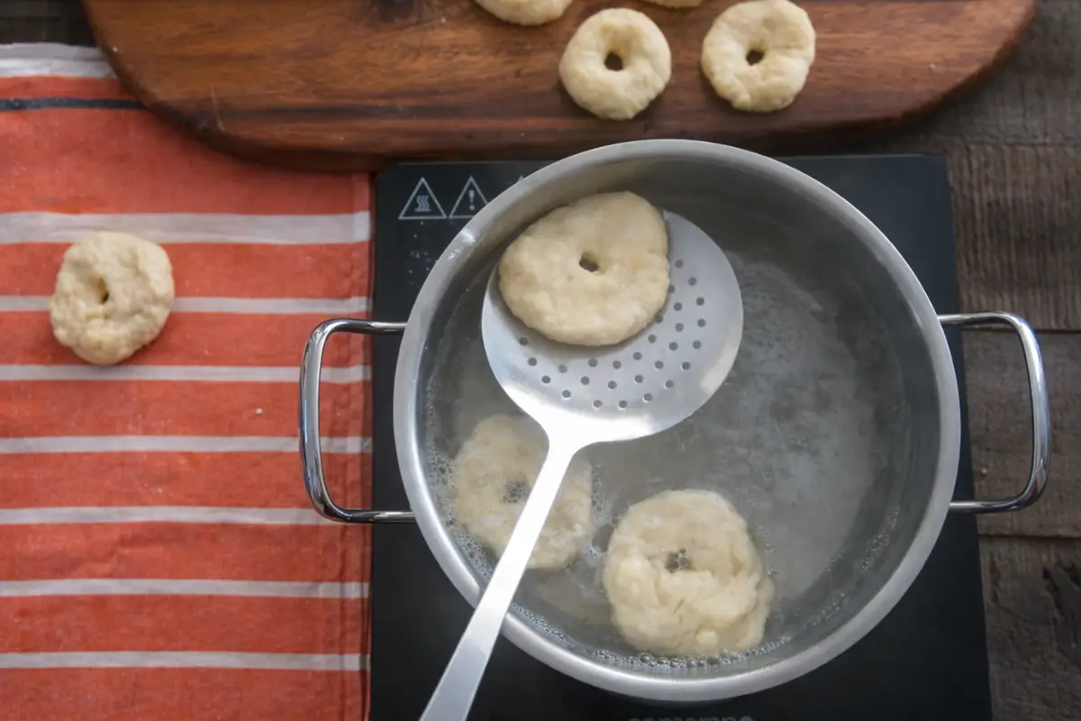 Dough rings boiling in water while being lifted with a slotted spoon.