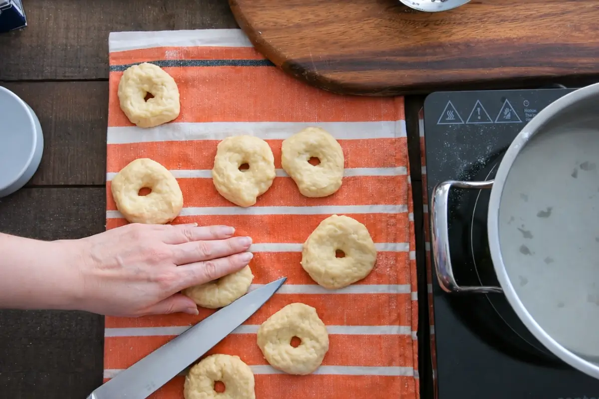 Knife making a side cut on shaped Taralli dough rings before baking.