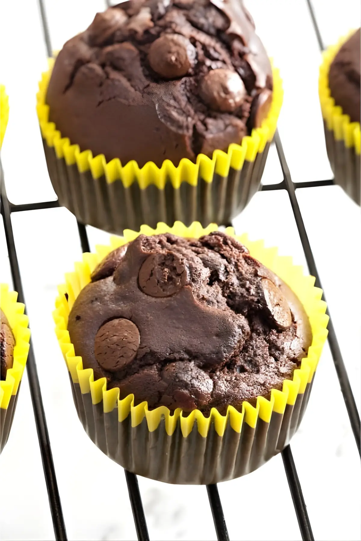 Close-up of a baked dairy-free chocolate muffin with chocolate chips on top in a yellow liner.