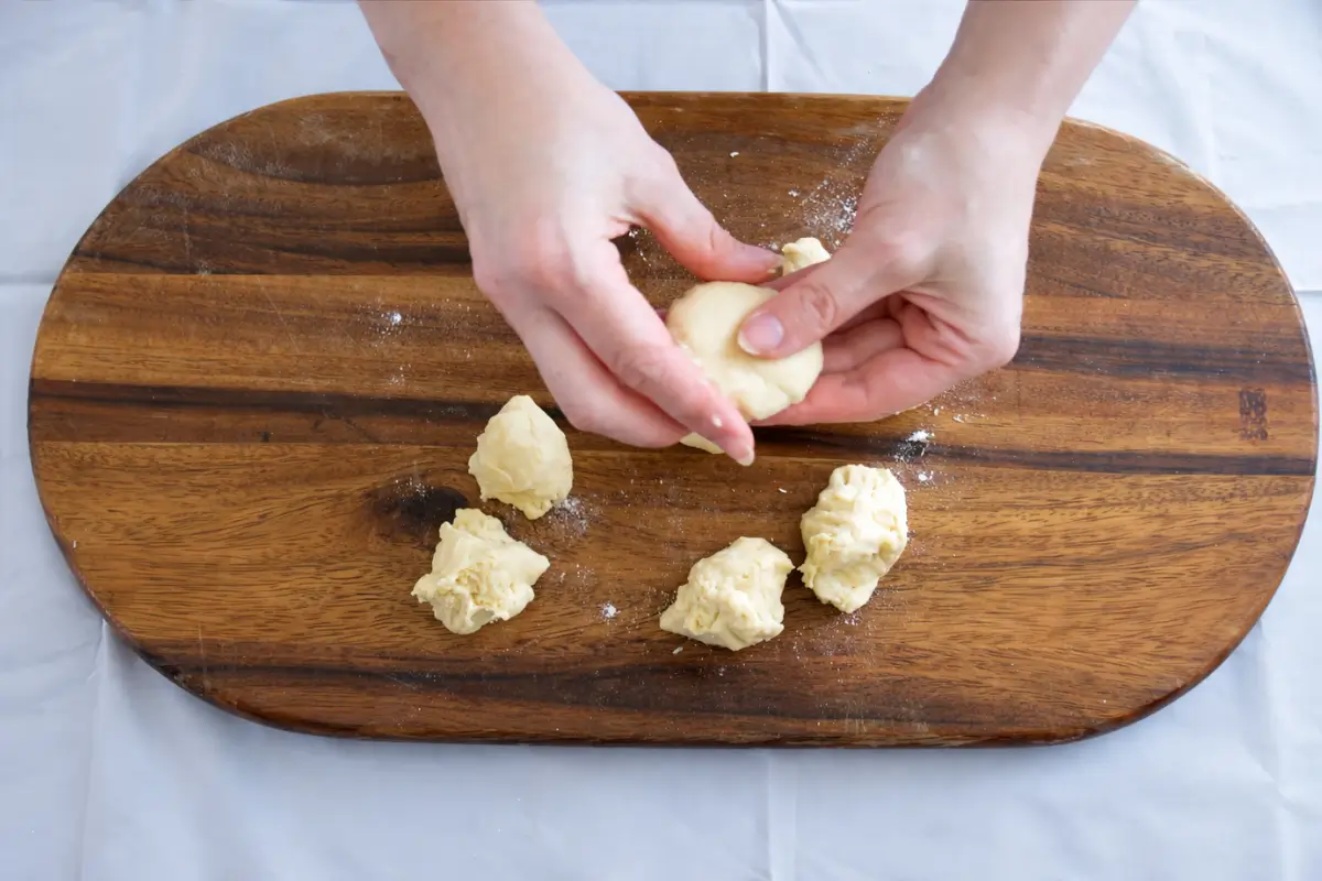 Hands flattening small pieces of taralli dough into patties on a wooden board.
