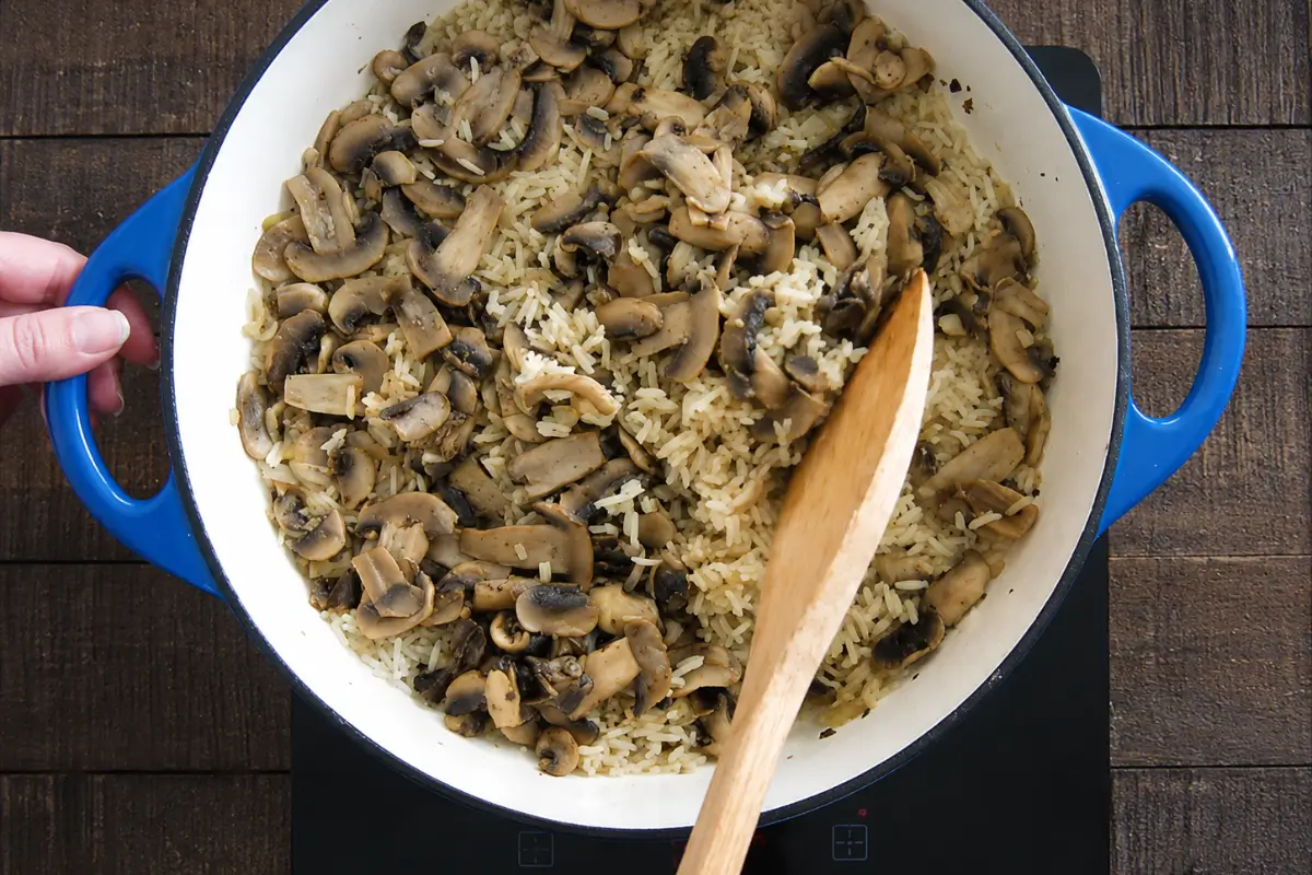 Fluffing cooked rice with mushrooms using a wooden spoon.