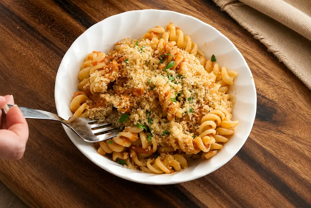 Fork lifting tuna pasta with garlic breadcrumbs from a serving bowl.