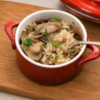 Mushroom rice with sliced mushrooms and chopped parsley served in a red dish.