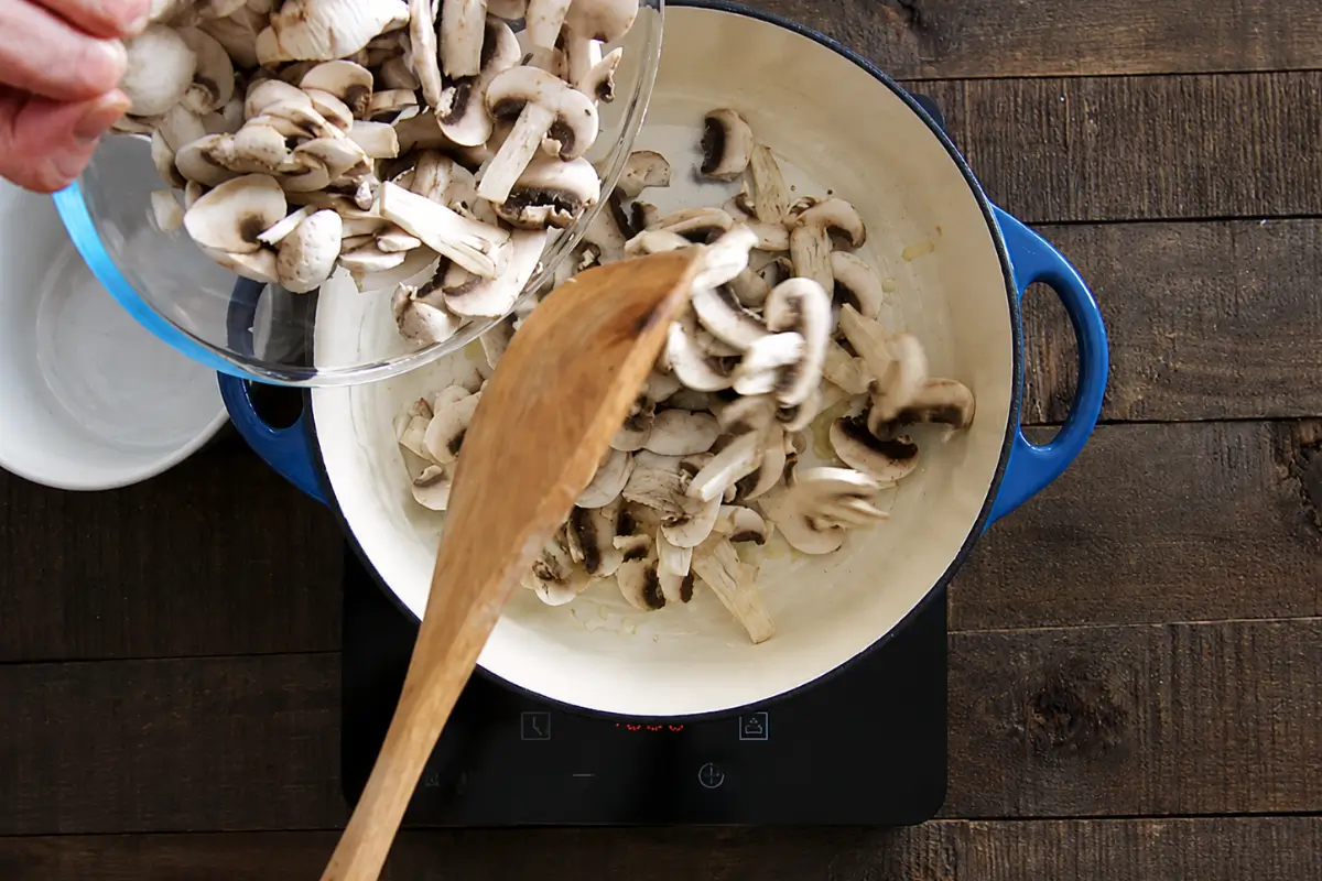 Sliced mushrooms being added to the pot with onion and garlic.