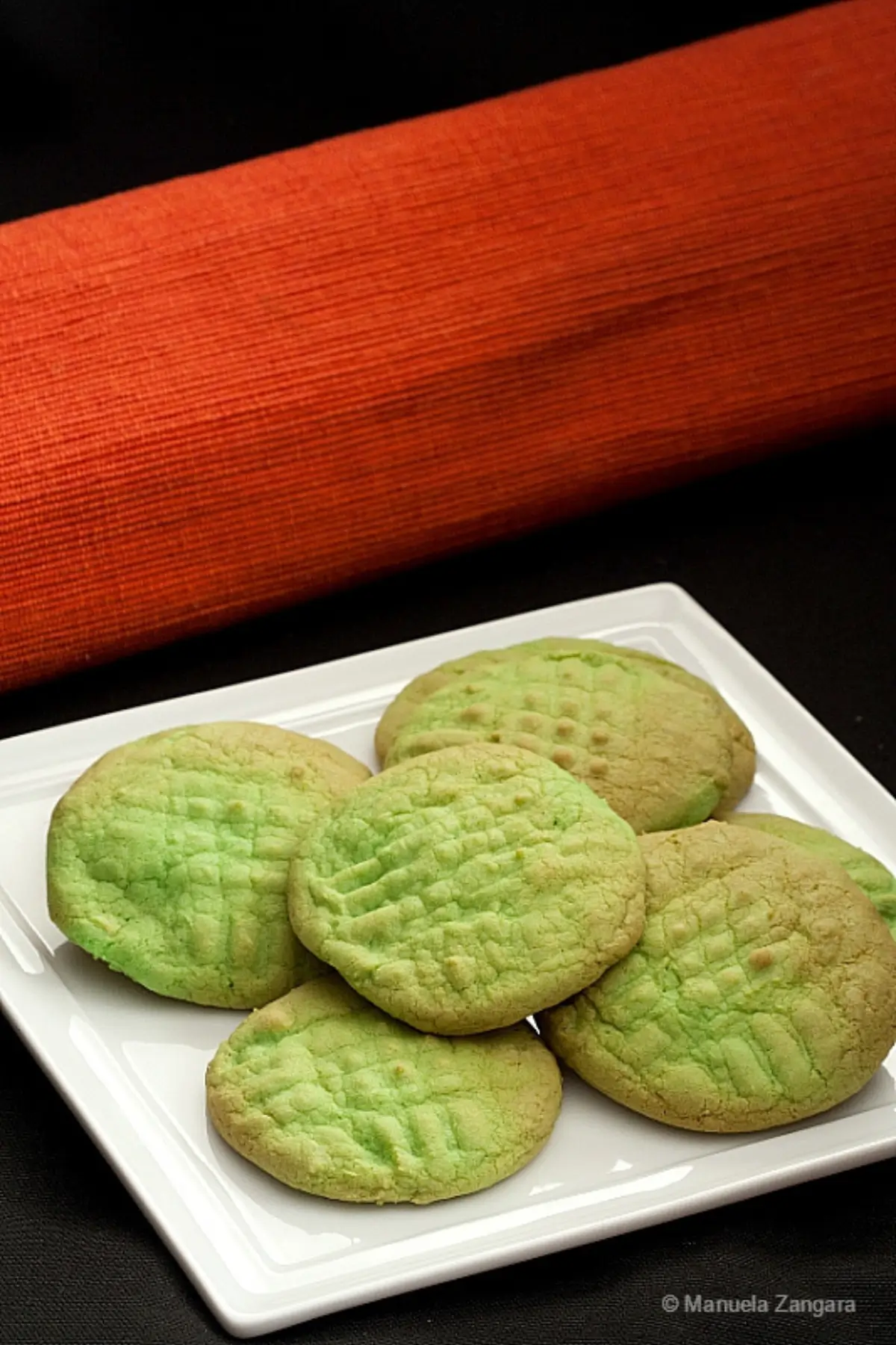 Soft green vanilla cookies with lightly browned tops served on a white plate.