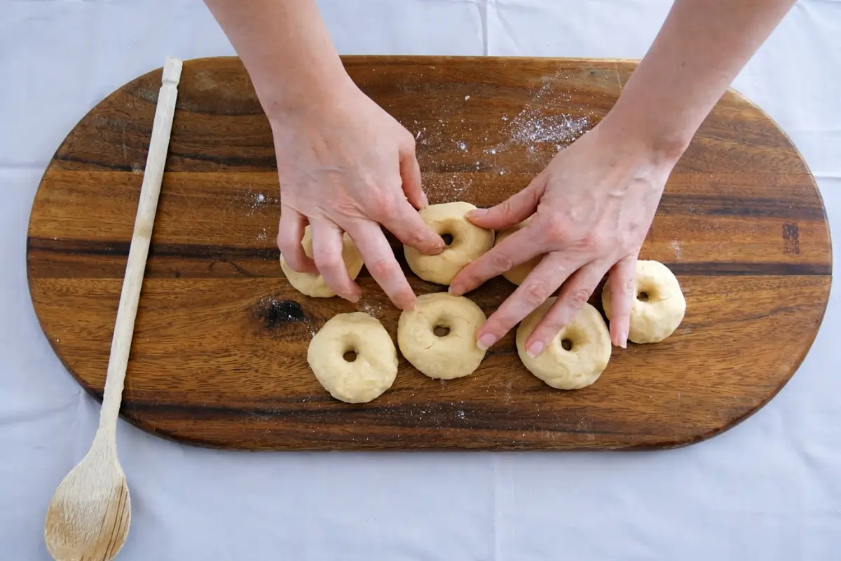 Hands pressing holes into dough pieces to form Italian Taralli rings.
