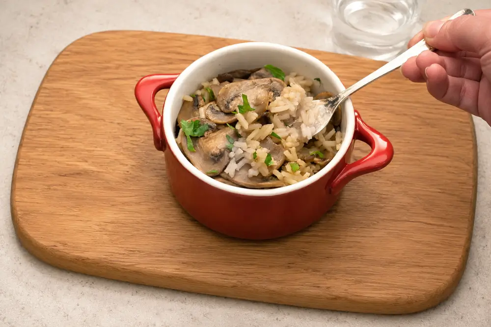 A spoon lifting fluffy rice and sliced mushrooms from a red serving dish.