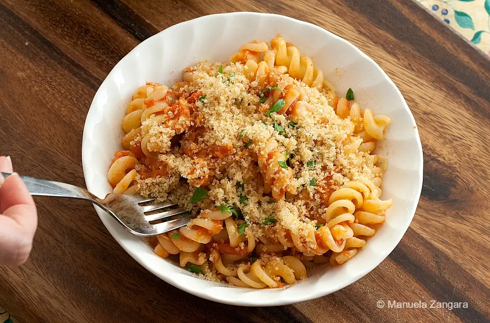 Bowl of tuna tomato pasta with garlic breadcrumbs as a fork lifts a bite.