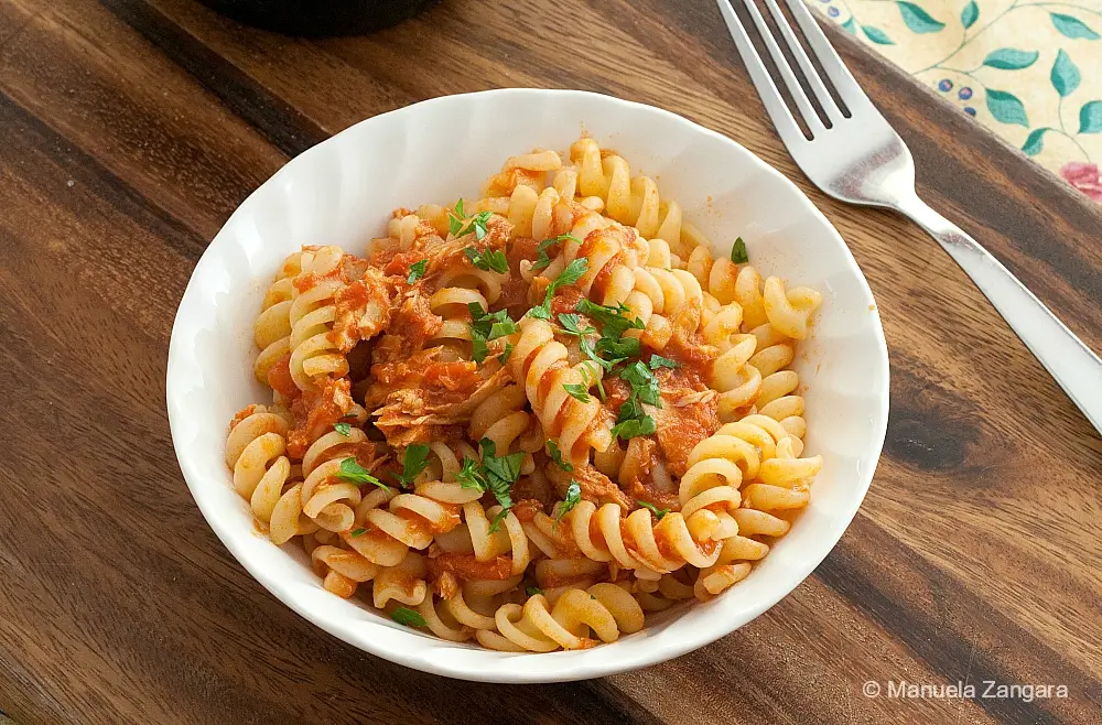 Bowl of tuna tomato pasta topped with garlic breadcrumbs and parsley.