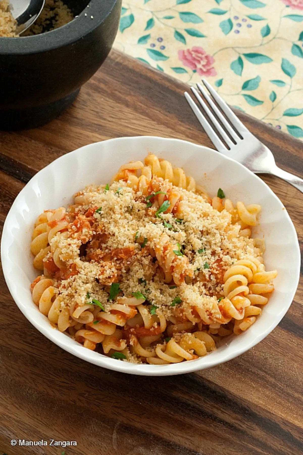Bowl of tuna tomato pasta with garlic breadcrumbs as a fork lifts a bite.