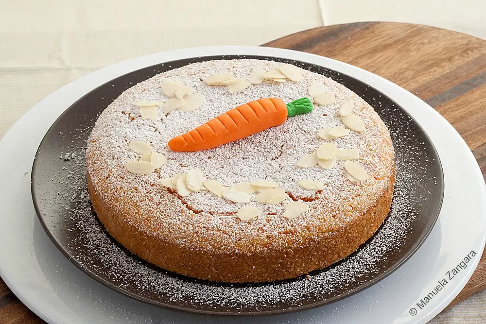 Whole almond carrot cake decorated with a fondant carrot and almond flakes.