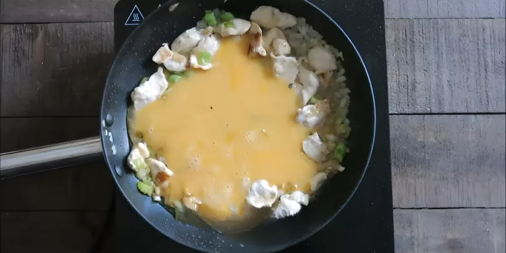 Beaten eggs poured into the wok beside the cooked chicken and vegetables.