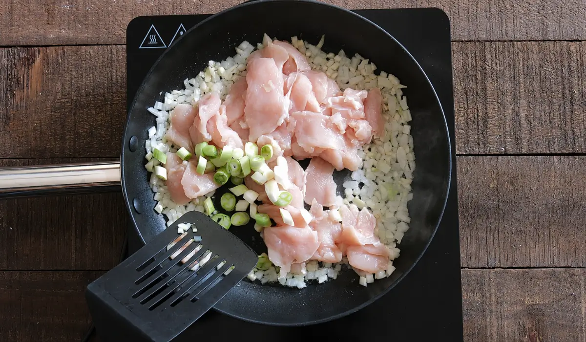 Chicken, onions, and green onions cooking in a pan before adding rice.