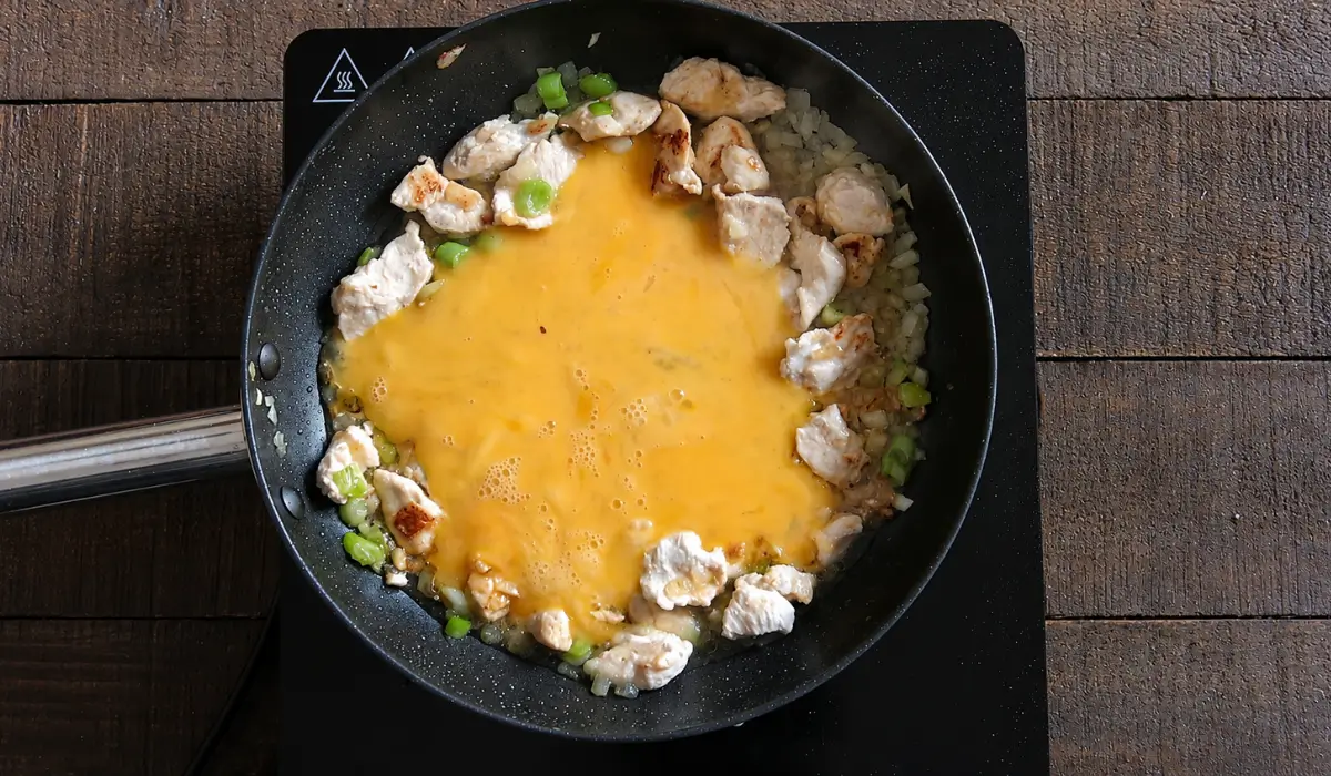 Beaten eggs cooking with chicken, onions, and green onions for Thai chicken fried rice.
