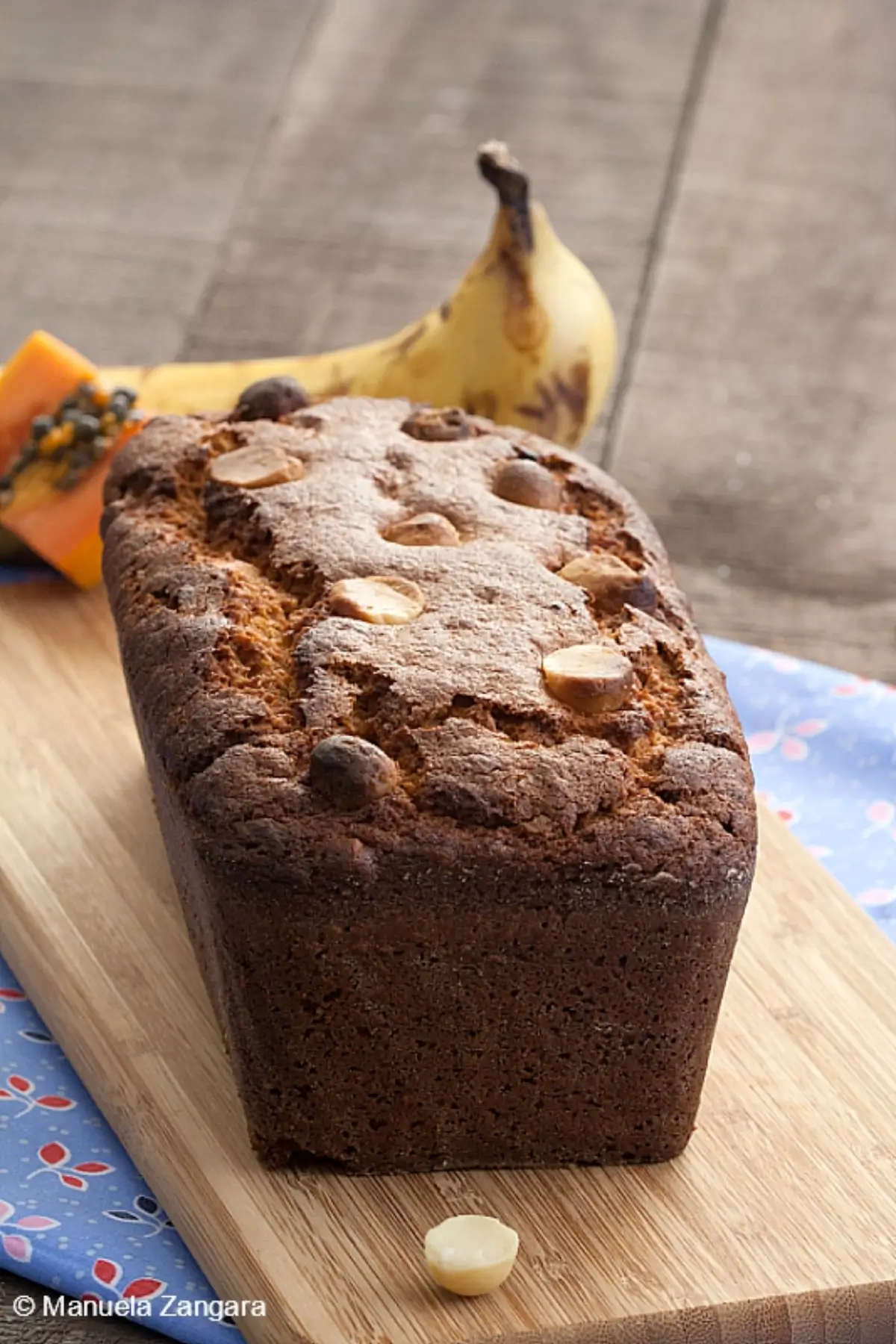 Papaya banana bread loaf with golden crust and macadamias on top.