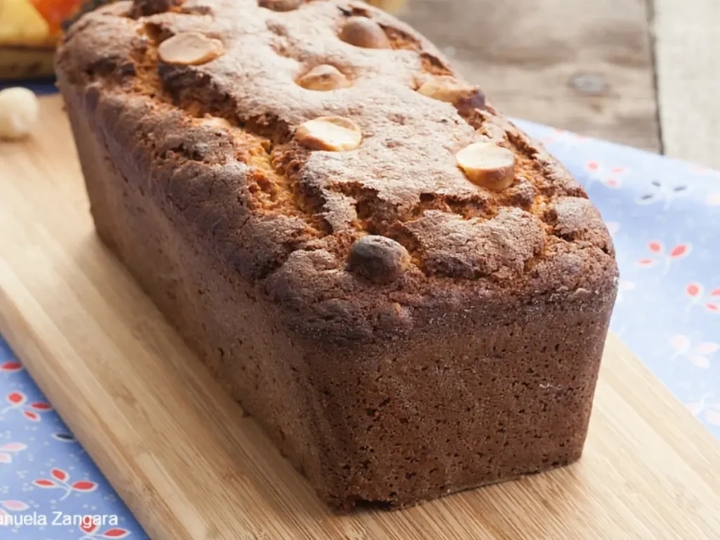 Whole papaya banana bread loaf topped with macadamias on a wooden board.