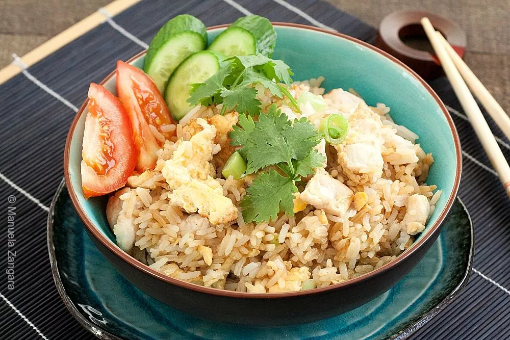 Close-up of Thai chicken fried rice topped with coriander and served with cucumber and tomato slices.