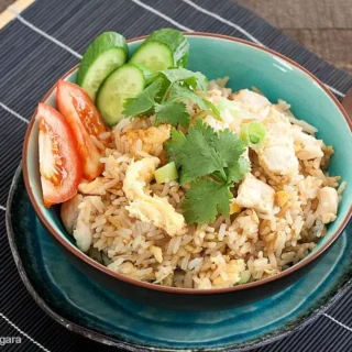 Bowl of Thai chicken fried rice garnished with cucumber, tomato, and coriander.