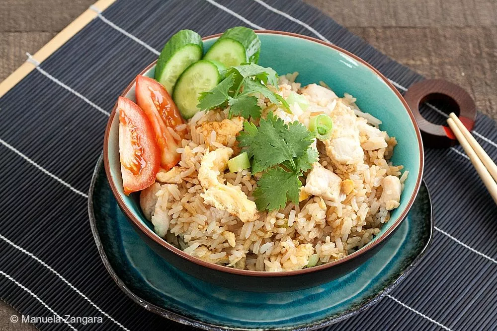 Bowl of Thai chicken fried rice garnished with cucumber, tomato, and coriander.