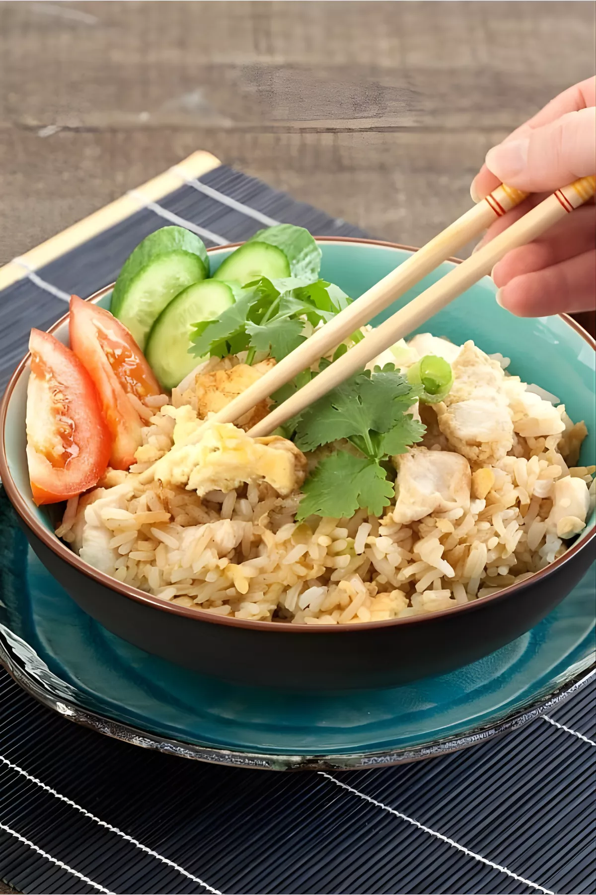 Hand using chopsticks to pick up Thai chicken fried rice with egg and coriander.