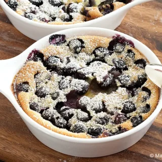 Blueberry Clafoutis baked in a white ceramic dish, dusted with icing sugar and filled with whole berries.