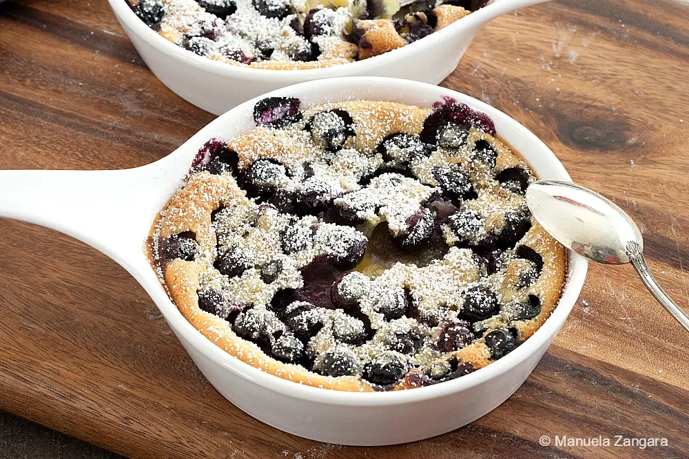 Blueberry Clafoutis baked in a white ceramic dish, dusted with icing sugar and filled with whole berries.