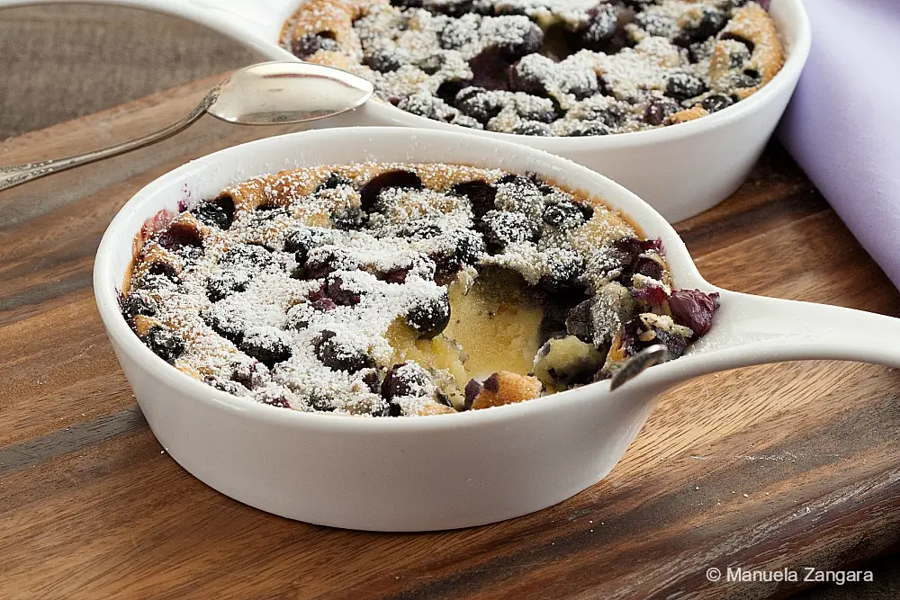 Baked custard dessert topped with blueberries and a light coating of icing sugar.