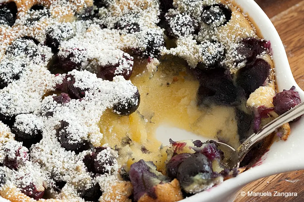 Close-up of golden baked custard with juicy blueberries and powdered sugar.